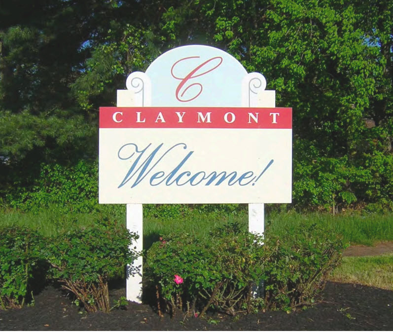 Welcome sign in Claymont, Delaware in front of green trees and flowering bushes.