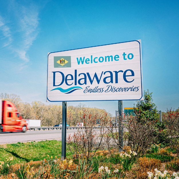 Welcome to Delaware highway sign along with the seal from the Delaware State Flag superimposed on the sign.